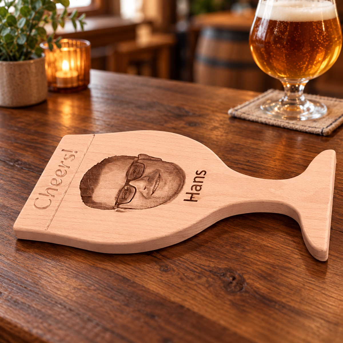 Beukenhouten borrelplank van DecoSpace in de vorm van een speciaalbierglas, met ingefreesd ‘Cheers!’, een gegraveerd portret en de naam Hans, met speciaalbier op de achtergrond.