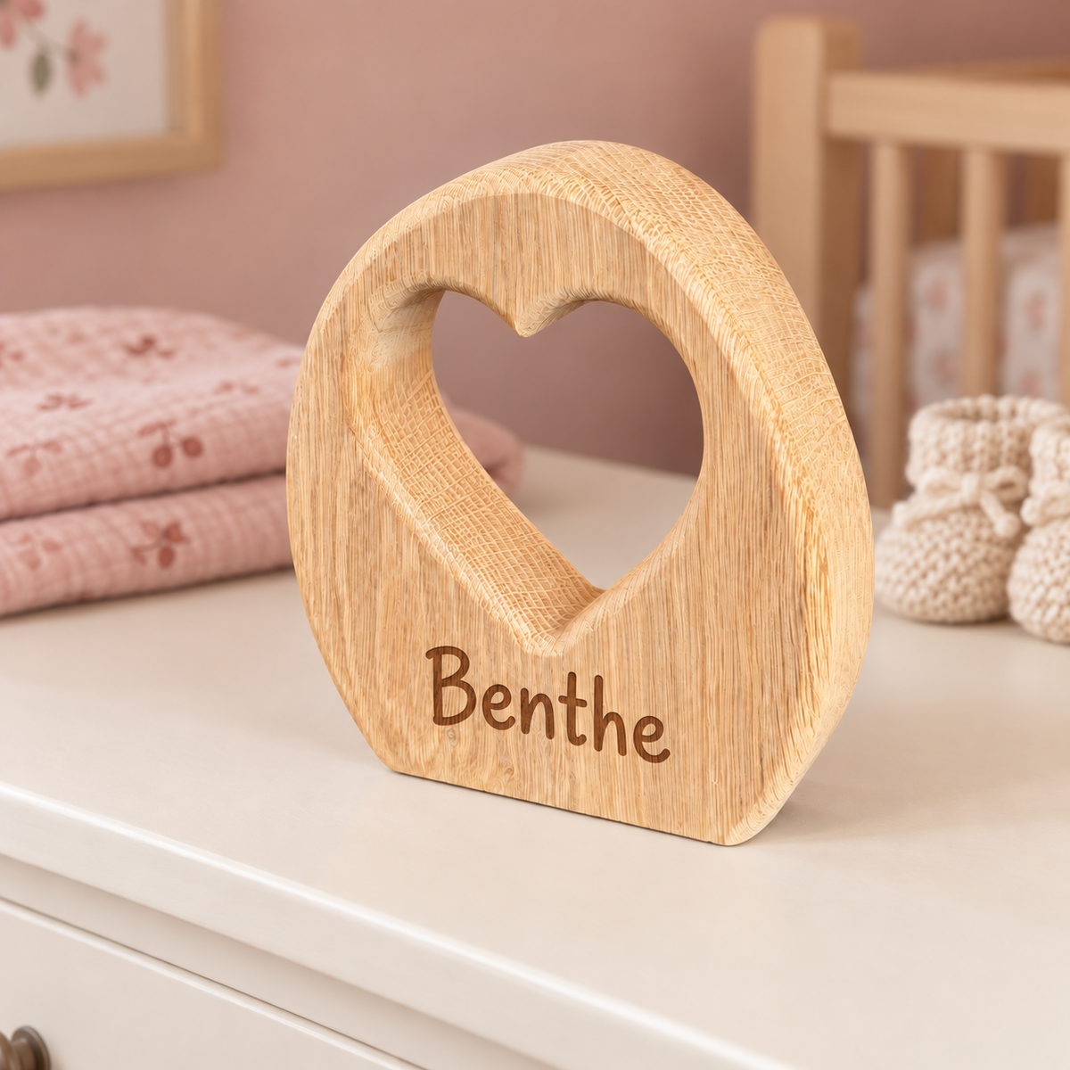 Eiken decoratie van DecoSpace met hartvormige uitsparing en de naam Benthe in speelse losse letters, op een witte commode in een zachtroze babykamer.