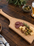 Roeiriem borrelplank van massief beukenhout met sapgeul, sfeervol gepresenteerd met kaas, salami, olijven en noten op een rustieke houten tafel met een glas bier.