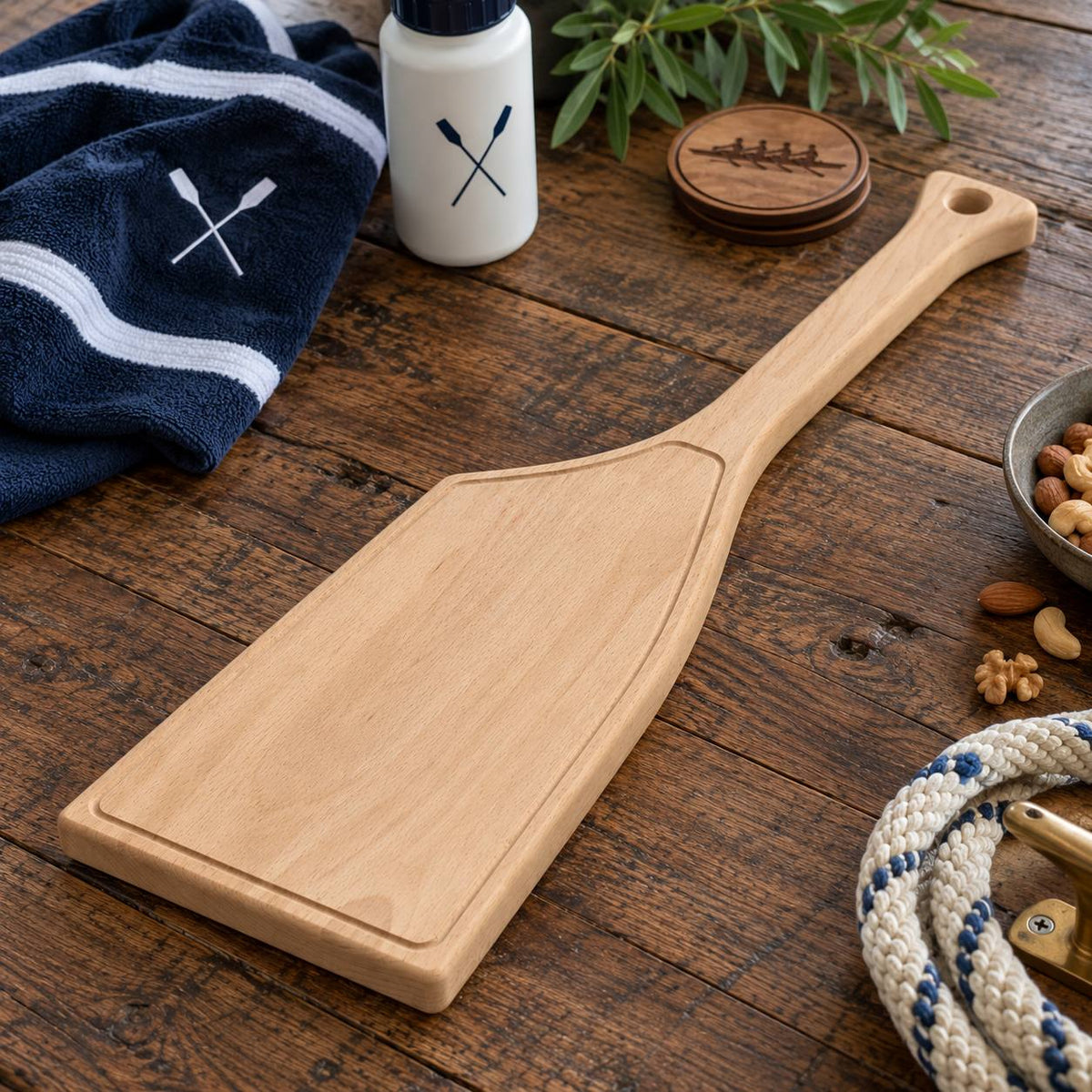 Ongepersonaliseerde roeiriem borrelplank van massief beukenhout met gefreesde sapgeul en ophanggat, gepresenteerd op een rustieke houten tafel met roeisportaccessoires.