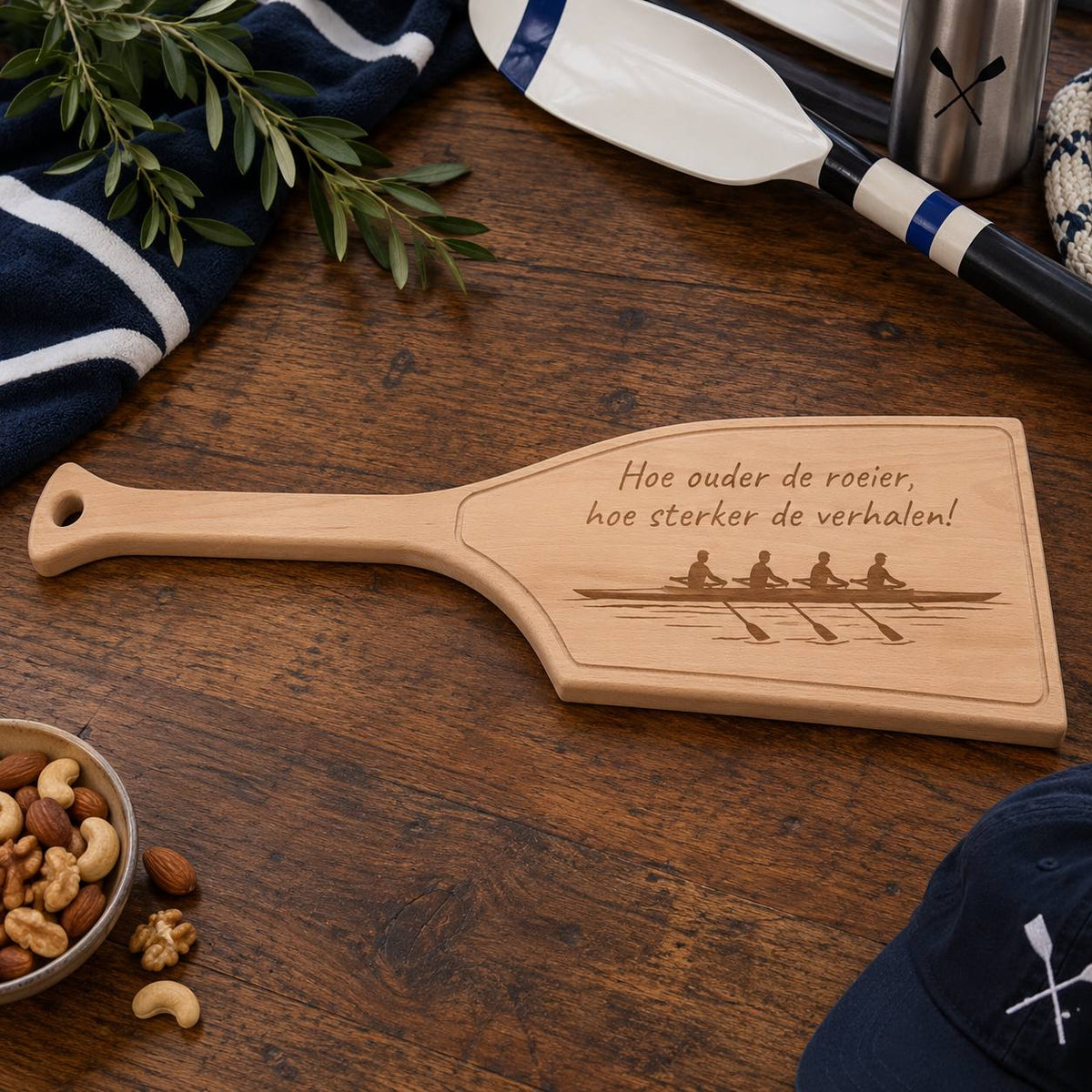 Gepersonaliseerde roeiriem borrelplank van massief beukenhout met lasergravure van vier roeiers en de tekst ‘Hoe ouder de roeier, hoe sterker de verhalen!’, sfeervol gepresenteerd op een houten tafel.