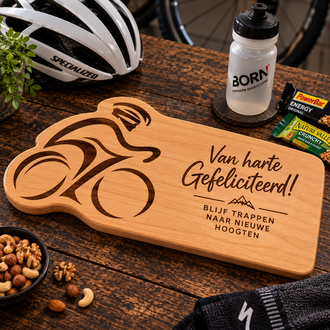 Massief beukenhouten borrelplank voor wielrenners met gegraveerde wielrenner en felicitatietekst, gefotografeerd met fietshelm, bidon en sportrepen.